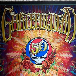 May include: A vibrant poster featuring the words "Grateful Dead" in gold lettering. The artwork includes a skull with a "50" in a circle, surrounded by roses. The background is a colorful mix of reds, oranges, and blues, with a border of green vines.
