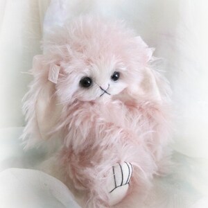 Può includere: Un coniglietto di peluche morbido e rosa, con orecchie bianche e un fiocco bianco. Il coniglietto ha occhi neri e un naso nero.