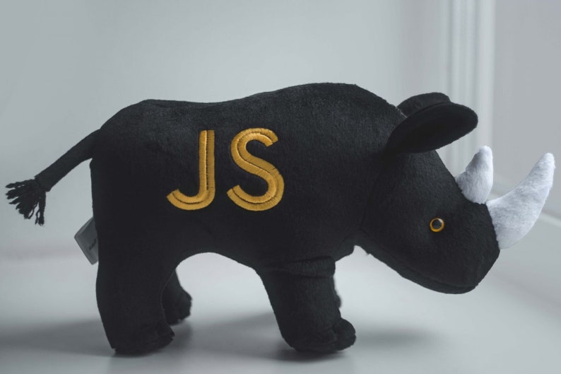 May include: Black plush rhinoceros toy with a white horn and gold embroidered initials "JS".