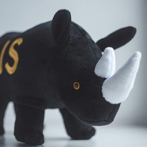 May include: Black plush rhinoceros toy with a white horn and a gold embroidered letter 'S' on its side.
