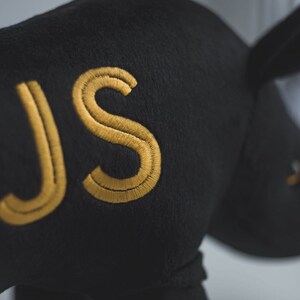 May include: Black plush rhinoceros toy with the letters "JS" embroidered in gold thread.