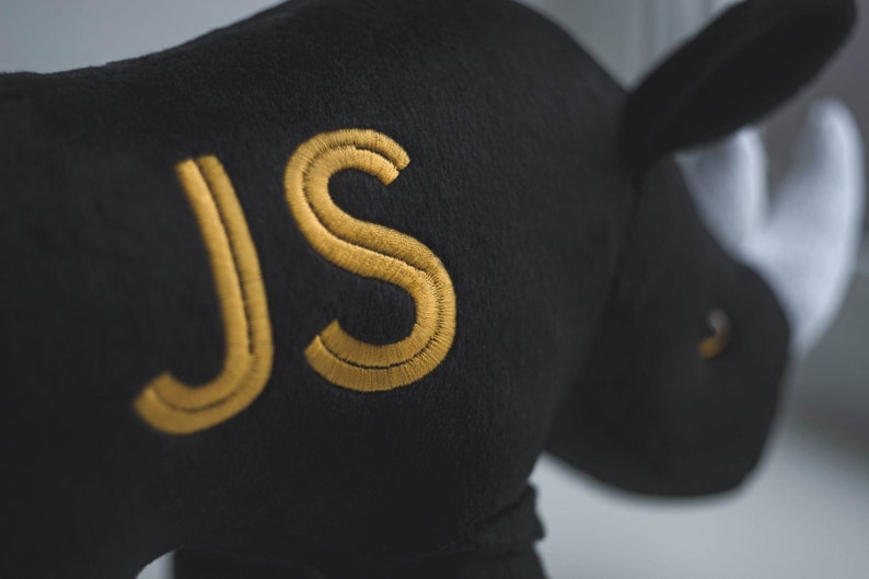 May include: Black plush rhinoceros toy with the letters "JS" embroidered in gold thread.