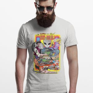 May include: White t-shirt featuring a colorful comic book-style graphic. The graphic includes an alien, a car, and the text "Lost Valley". The design has a retro, vintage aesthetic.
