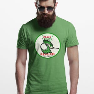 May include: Green t-shirt with a retro graphic. The design is circular, featuring a green dinosaur-like creature and the words "REBEL ROAD" and "GASOLINE". The shirt is a solid green colour.