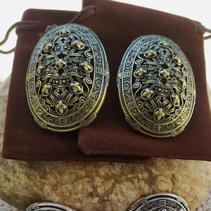 Puede incluir: Cuatro broches de metal ovalados adornados con diseños intrincados. Dos son de color dorado y dos son de color plateado.