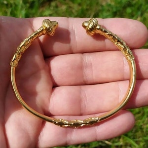 May include: A gold-toned bangle bracelet with a twisted design and decorative knots at each end.