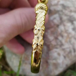 May include: A gold bangle bracelet with a textured design. The bracelet has a floral pattern and a round knob at the top.