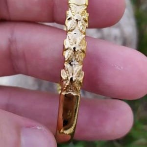 May include: A gold bangle bracelet with a floral design. The bracelet is made of a smooth, shiny metal and has a simple, elegant design.