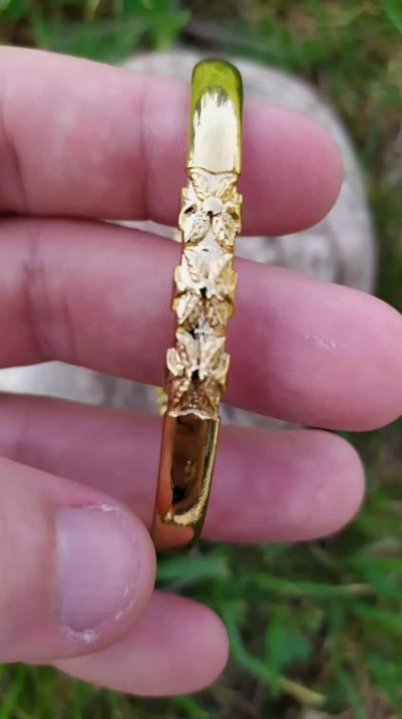 May include: A gold bangle bracelet with a floral design. The bracelet is made of a smooth, shiny metal and has a simple, elegant design.