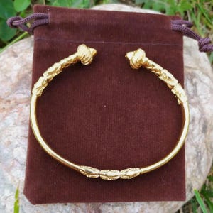 May include: A gold bangle bracelet with a decorative design. The bracelet has a smooth, rounded surface and is adorned with intricate details.