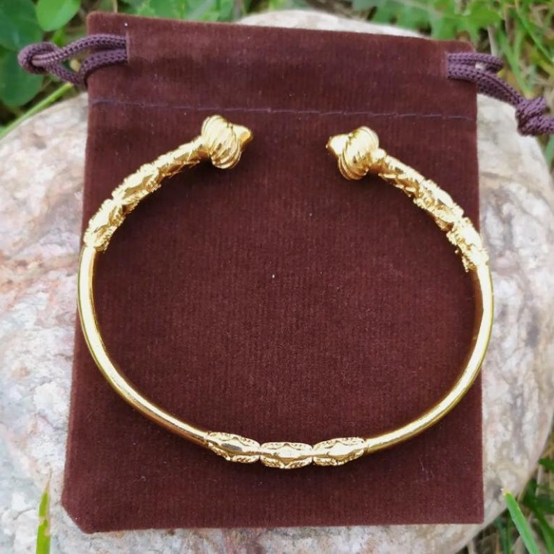 May include: A gold bangle bracelet with a decorative design. The bracelet has a smooth, rounded surface and is adorned with intricate details.