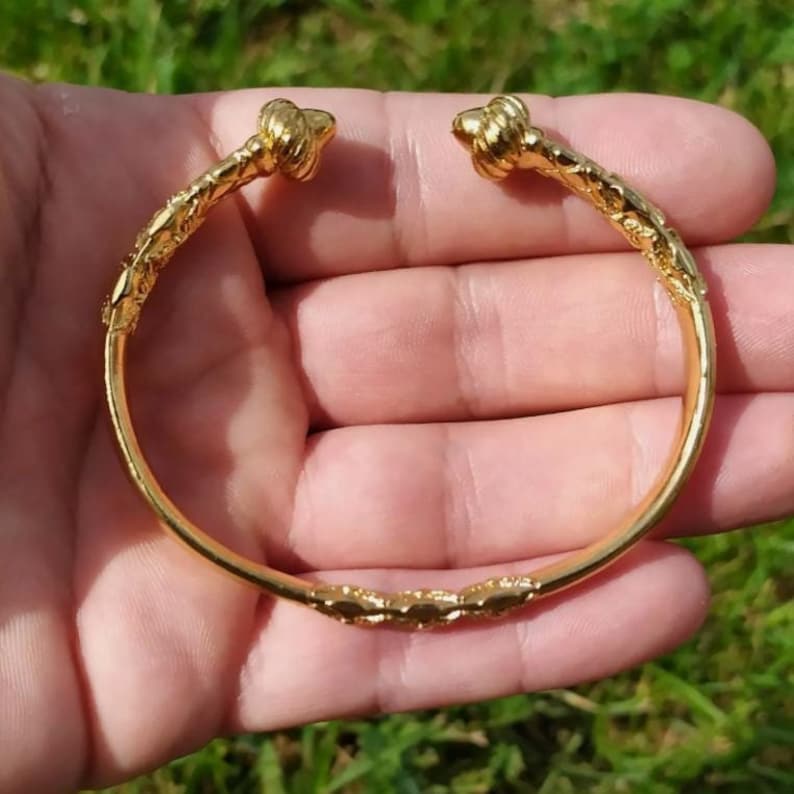 May include: A gold-toned bangle bracelet with a twisted design and decorative knots at each end.