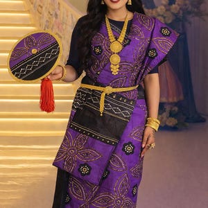 Puede incluir: Un sari morado y negro con patrones florales de cuentas doradas, un tocado a juego y un abanico circular con una borla roja. El conjunto incluye un collar dorado, un cinturón dorado y brazaletes dorados sobre una blusa azul marino oscuro.