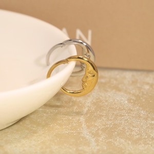 May include: Two hoop earrings, one gold-toned and one silver-toned, each featuring a crescent moon design with a detailed human face embossed on the surface. The earrings are circular in shape and have a polished, metallic finish throughout.