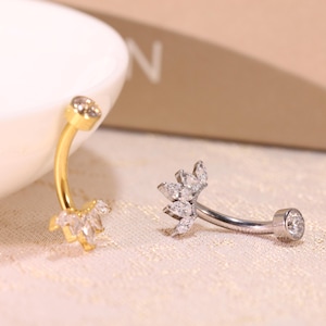 Puede incluir: Dos anillos de ombligo con acentos de cristal transparente. El anillo de la izquierda es dorado y el anillo de la derecha es plateado.