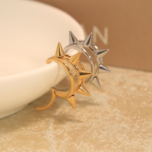 May include: Two hoop earrings featuring a series of pointed spikes along the outer edge. One earring is finished in a polished gold tone, while the other is finished in a polished silver tone. Both hoops have a circular design with sharp protrusions.
