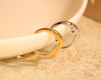 May include: Two crescent moon shaped hoop earrings, one gold and one silver, on a white surface.