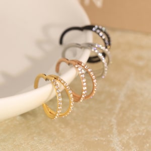 Può includere: Un set di tre orecchini a cerchio in tonalità oro, oro rosa e argento, ciascuno caratterizzato da un design a doppia fascia incastonato con piccole pietre chiare e scintillanti. Gli orecchini sono disposti in fila, mostrando le finiture.
