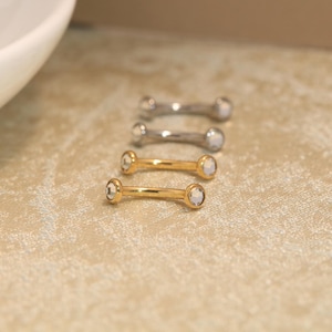 Peut inclure: Quatre bijoux de corps en forme de barre incurvée disposés en rangée. Deux pièces sont en métal argenté avec des extrémités circulaires transparentes, et deux pièces sont en métal doré avec des extrémités circulaires transparentes.