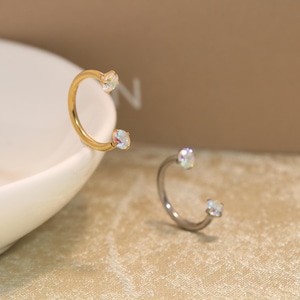 May include: Two horseshoe-shaped body jewellery rings, one in a gold tone and one in a silver tone. Each ring features a small, iridescent, round-cut gemstone set at both open ends, creating a symmetrical design with a polished metallic finish.