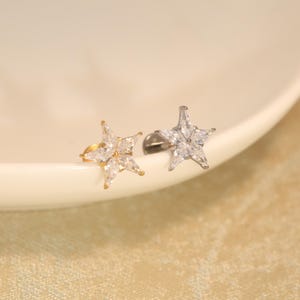 May include: Two star-shaped stud earrings featuring clear, marquise-cut cubic zirconia stones arranged in a star pattern. One earring has a gold-tone metal base, while the other has a silver-tone metal base, both with a flat back post closure.