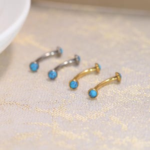 May include: Four curved barbell body jewellery pieces arranged in two pairs. Two barbells are dark grey metal and two are gold-toned metal. Each end of the curved bars features a small, round, bright turquoise stone with subtle dark veining.