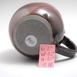 May include: A brown ceramic mug with a handle. The mug is 5 inches long, 3.5 inches wide, and 3.5 inches high. It weighs 12 ounces. The bottom of the mug has a white sticker with the number "M021" written on it.