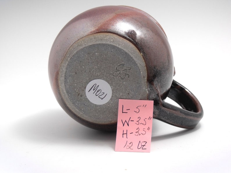 May include: A brown ceramic mug with a handle. The mug is 5 inches long, 3.5 inches wide, and 3.5 inches high. It weighs 12 ounces. The bottom of the mug has a white sticker with the number "M021" written on it.