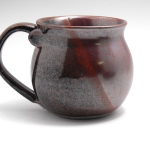 May include: A brown and gray ceramic mug with a rounded body and a handle. The mug has a speckled glaze.