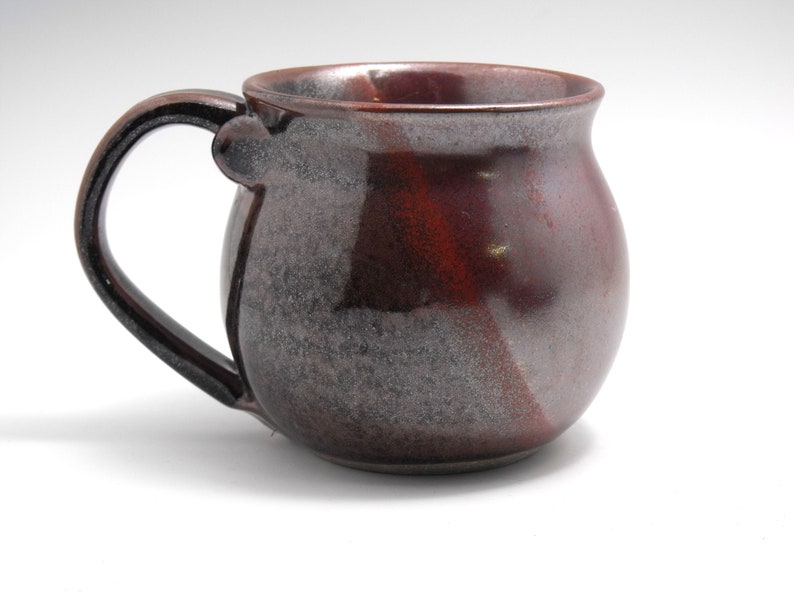 May include: A brown and gray ceramic mug with a rounded body and a handle. The mug has a speckled glaze.