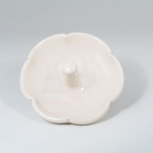May include: A white ceramic ring holder with a scalloped edge and a small center post.