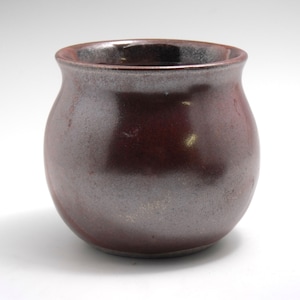 May include: A small, round, red and grey ceramic pot with a slightly flared rim.