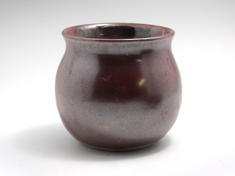 May include: A small, round, red and grey ceramic pot with a slightly flared rim.