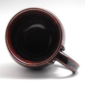 May include: A brown ceramic mug with a dark brown glaze and a black speckled handle. The mug is empty and the inside is visible.