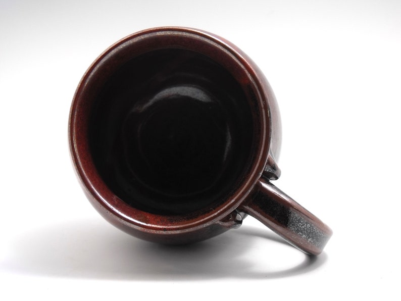 May include: A brown ceramic mug with a dark brown glaze and a black speckled handle. The mug is empty and the inside is visible.
