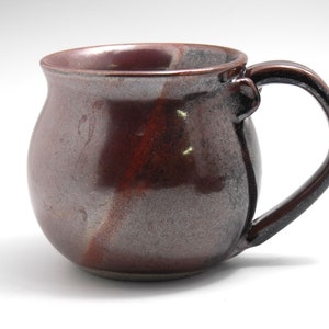 May include: A brown and grey ceramic mug with a rounded body and a handle. The mug has a speckled glaze.
