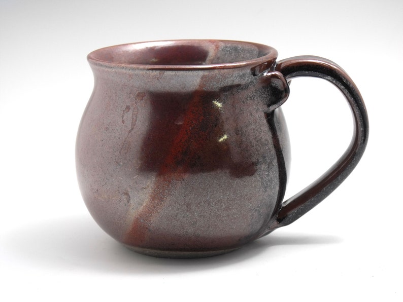 May include: A brown and grey ceramic mug with a rounded body and a handle. The mug has a speckled glaze.