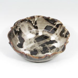 May include: A white ceramic bowl with a brown and black glaze. The bowl has a scalloped edge and a unique abstract design.