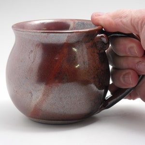 May include: A brown and white ceramic mug with a rounded body and a black handle. The mug has a speckled glaze and a slightly uneven surface.