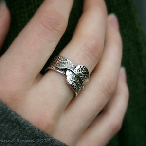 May include: A silver ring with a leaf design. The ring is made of two leaves that are intertwined and have a textured surface.