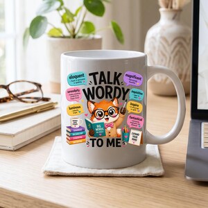 Può includere: Una tazza in ceramica bianca con un cartone animato di una volpe che indossa occhiali e papillon, che tiene un libro intitolato Big Words. Il testo Talk Wordy To Me è stampato sopra, circondato da fumetti colorati con vocaboli e definizioni.