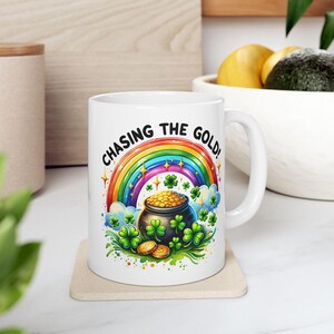 May include: White ceramic mug with a rainbow, pot of gold, and shamrocks. The text "Chasing the Gold!" is printed on the mug.