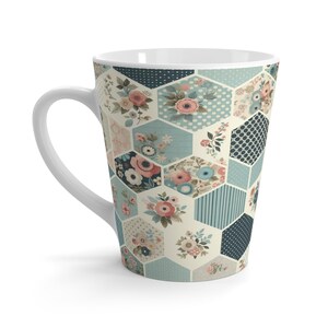 Pode incluir: Uma caneca de latte de cerâmica branca com um padrão hexagonal com desenhos florais em tons de rosa, azul e verde. A caneca tem uma alça branca.
