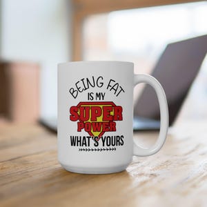 May include: White ceramic coffee mug with a red and yellow superhero logo and the text "Being fat is my super power what's yours".