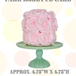 May include: A fake rosette cake on a green cake stand. The cake is decorated with pink frosting and is approximately 4.75 inches wide and 4.75 inches high.