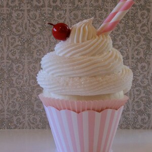 May include: A pink and white striped cupcake with white frosting and a red cherry on top. A pink and white striped straw is sticking out of the frosting.