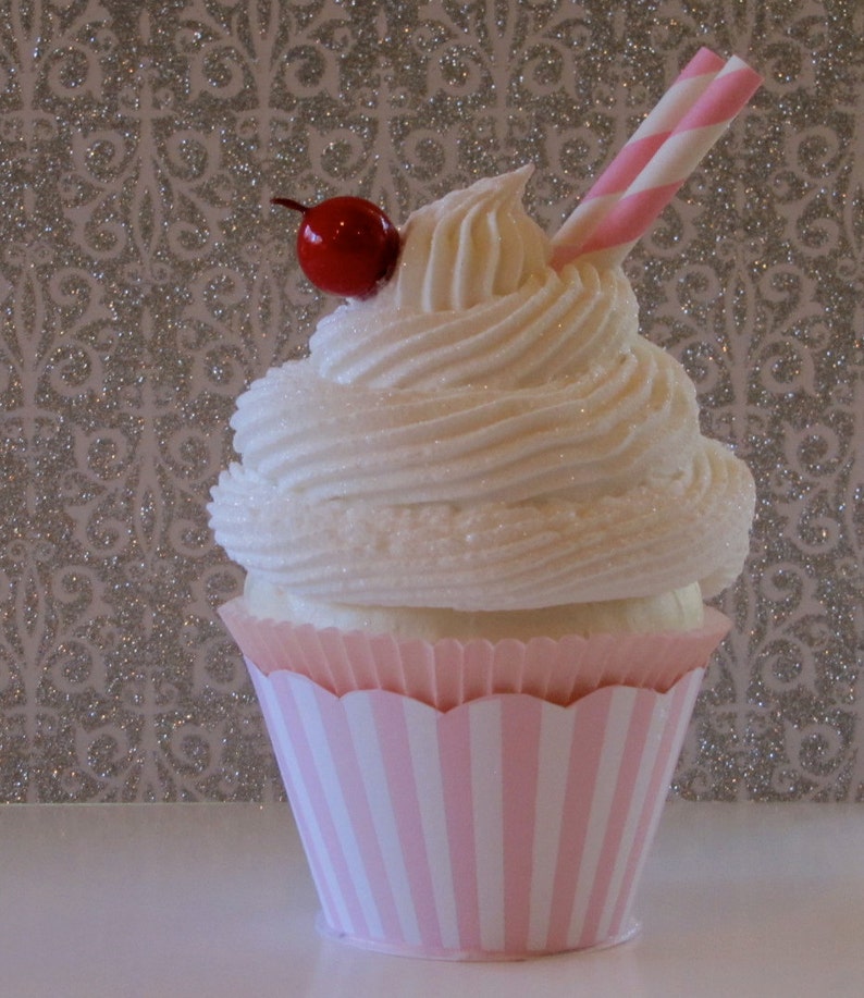 May include: A pink and white striped cupcake with white frosting and a red cherry on top. A pink and white striped straw is sticking out of the frosting.