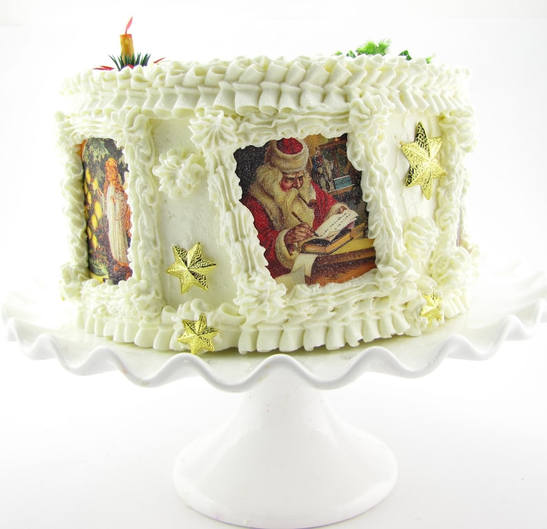 K&ouml;nnte beinhalten: Ein wei&szlig;er Kuchen, verziert mit wei&szlig;em Frosting und goldenen Sternen. Der Kuchen hat Bilder von Weihnachtsmann und Engeln an den Seiten.