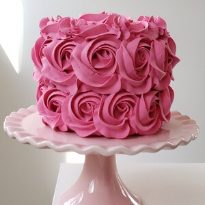 Puede incluir: Un pastel rosa decorado con rosas de glaseado rosa sobre un soporte para pastel rosa.