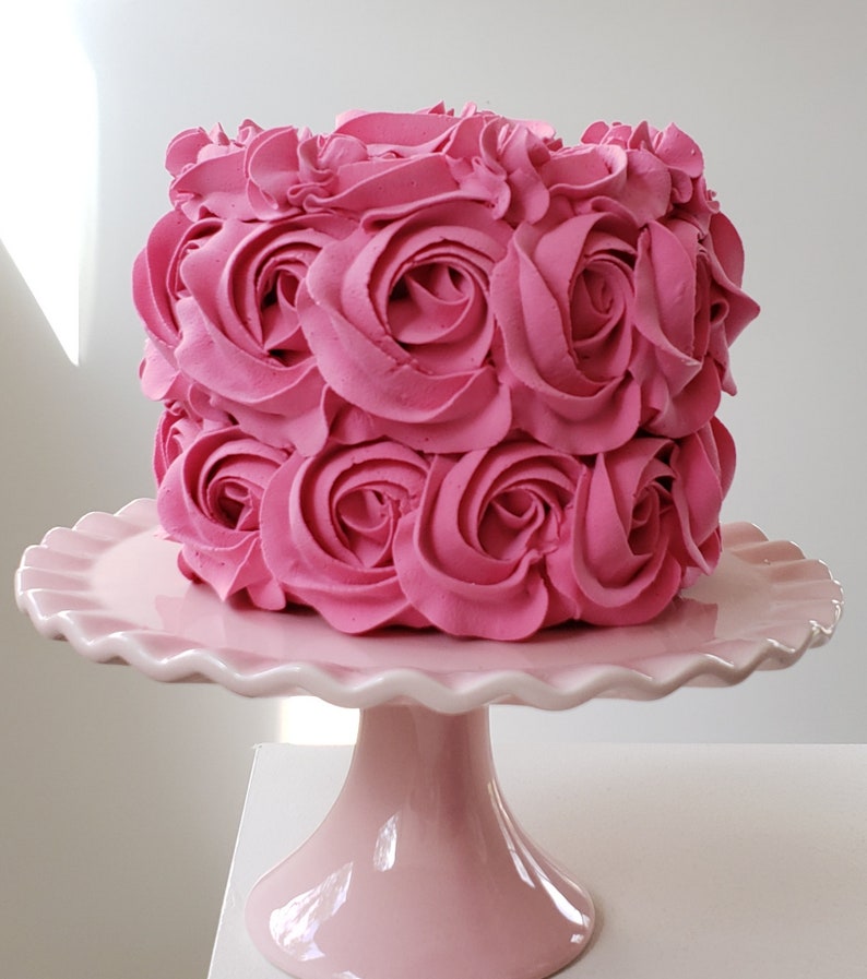 Puede incluir: Un pastel rosa decorado con rosas de glaseado rosa sobre un soporte para pastel rosa.